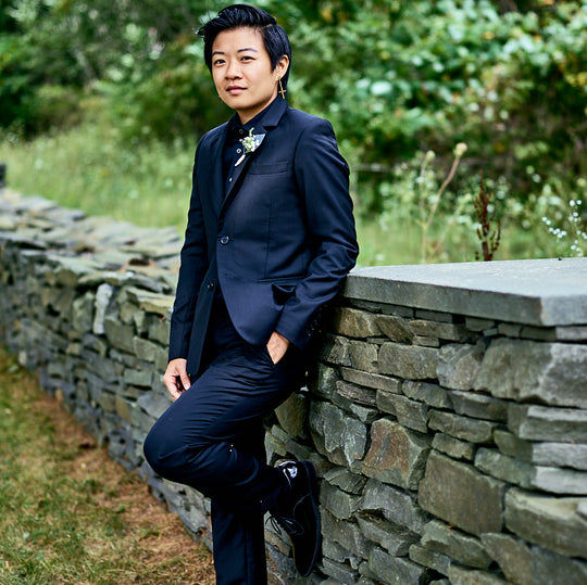 Model posted against a short stone wall wearing an all black suit by Kirrin Finch